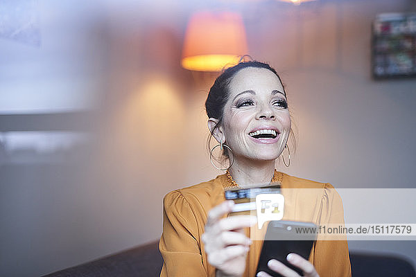 Glückliche Frau mit Smartphone und Kreditkarte zu Hause