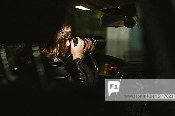 Junge Frau  die nachts mit einer Kamera aus einem Auto heraus fotografiert