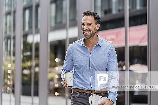 Businessman with takeaway coffee and newspaper in the city on the go