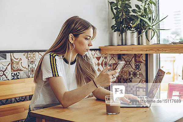 Junge Frau benutzt das Mobiltelefon und den Laptop im Café