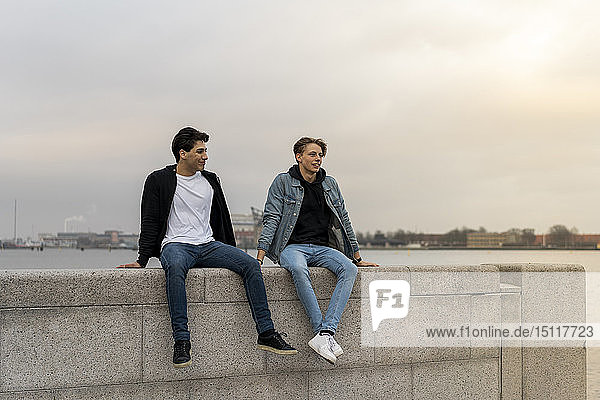 Denmark  Copenhagen  two young men sitting on wall at the waterfront