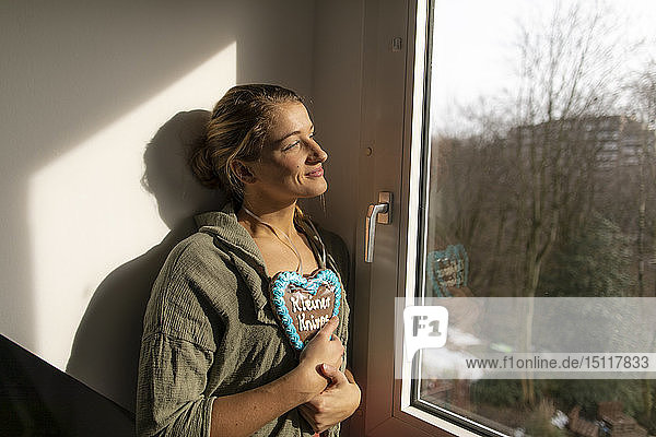 Lächelnde junge Frau am Fenster mit Lebkuchenherz
