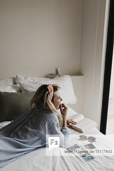 Junge Frau im Bett liegend mit Buch  Sonnenbrille und Polaroidbildern