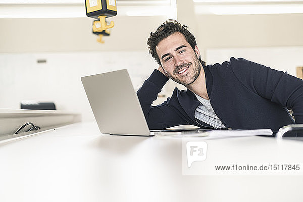 Relaxed young businessman with laptop  sitting in office