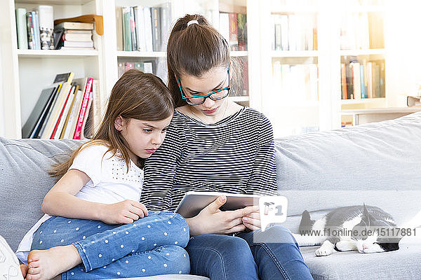 Zwei Schwestern sitzen zu Hause auf der Couch und schauen mit einem digitalen Tablet einen Film an