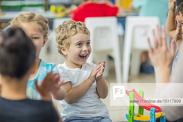 Glückliche Kinder und Vorschullehrerin klatschen im Kindergarten in die Hände