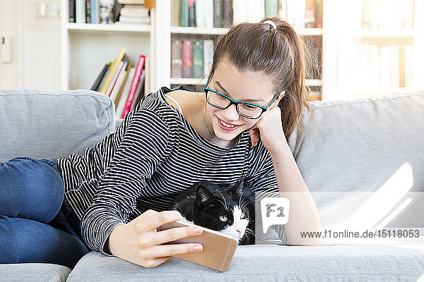 Smiling girl lying on couch at home taking selfie with cat