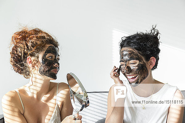 Zwei glückliche junge Frauen tragen zu Hause Gesichtsmasken auf