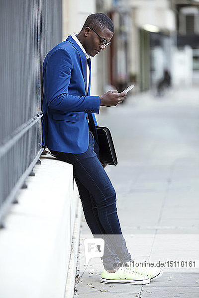 Junger Geschäftsmann in blauer Anzugsjacke und mit Smartphone