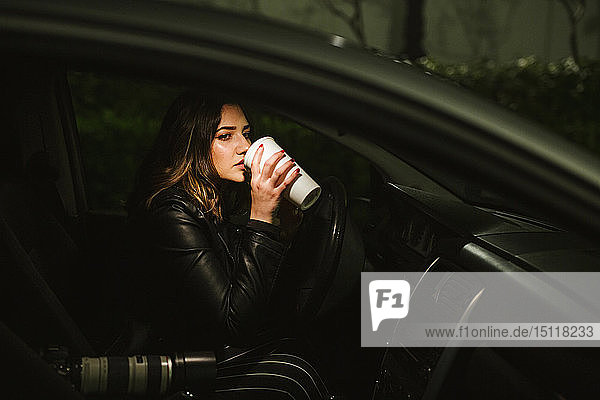 Young woman with disposable cup and camera in a car at night
