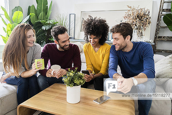 Vier glückliche Freunde sitzen auf der Couch und telefonieren
