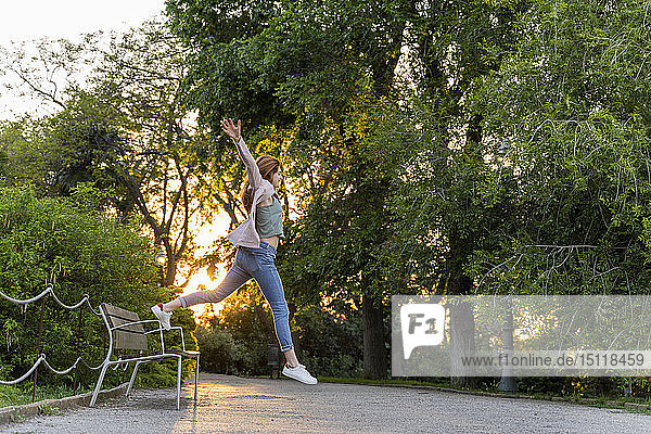Junge rothaarige Frau springt in einem Park von einer Bank