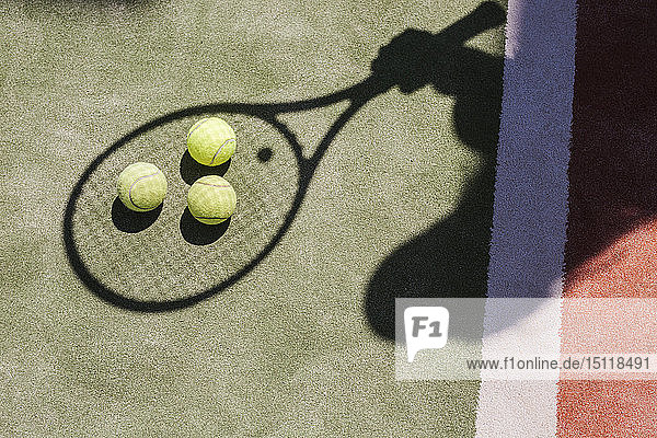 Schatten eines Tennisspielers mit Bällen und Schläger auf dem Platz