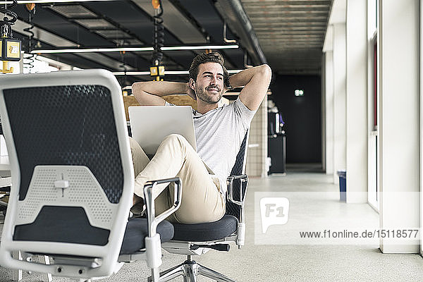 Young businessman working relaxed in modern office  with laptop on lap