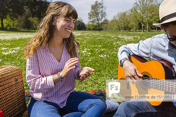 Junger Mann spielt Gitarre für seine Freundin in einem Park