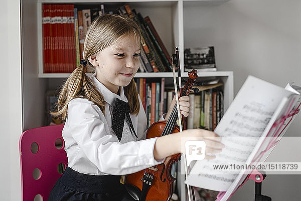 Lächelndes Mädchen mit Violine betrachtet Noten auf dem Notenständer
