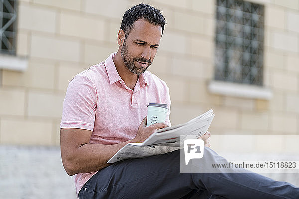 Mann mit Kaffee zum Mitnehmen liest Zeitung in der Stadt