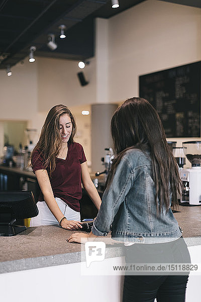 Junge Frau bezahlt bargeldlos mit Kreditkarte an der Theke eines Cafés