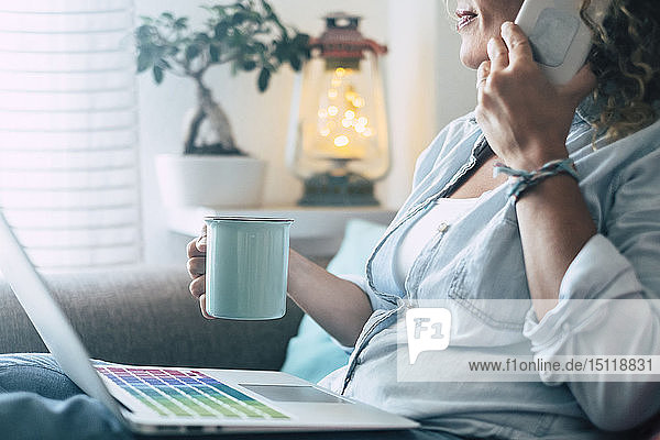 Nahaufnahme einer Frau auf der Couch zu Hause mit Kaffeetasse  Laptop und Mobiltelefon