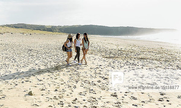 Drei Frauen mit Gitarre gehen am Strand spazieren