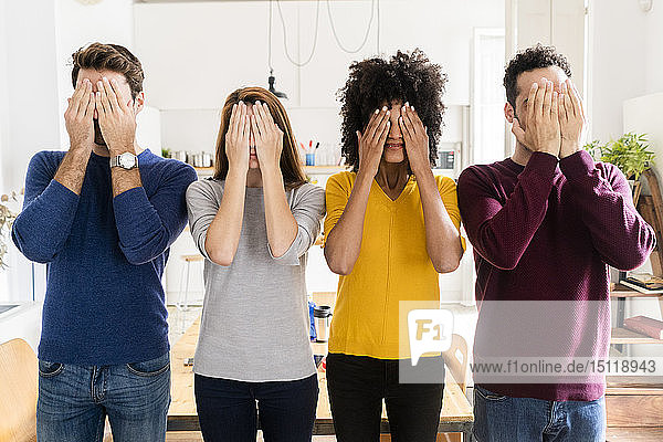 Four friends standing side by side at home covering their faces