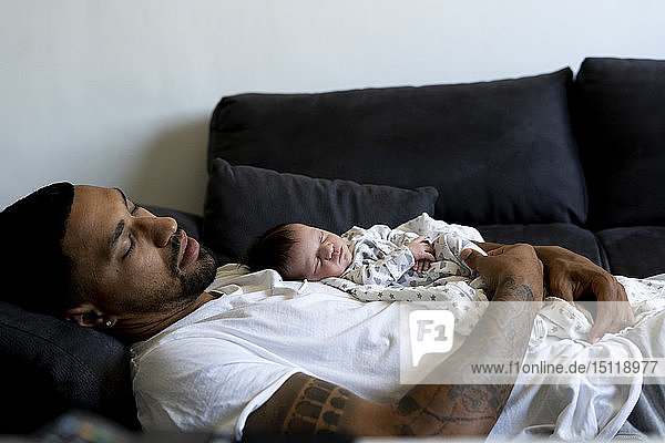 Father with newborn baby sleeping on couch
