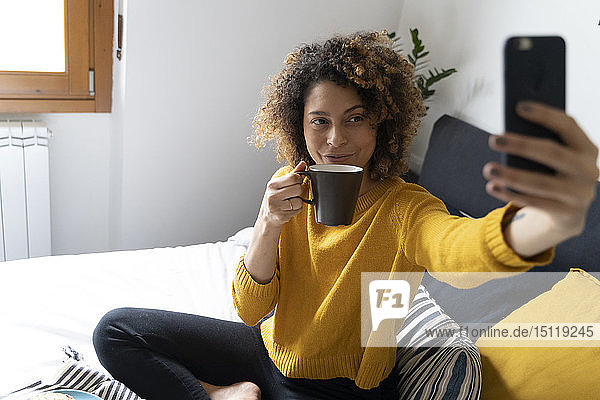Woman sitting on bed  taking selfies  drinking coffee