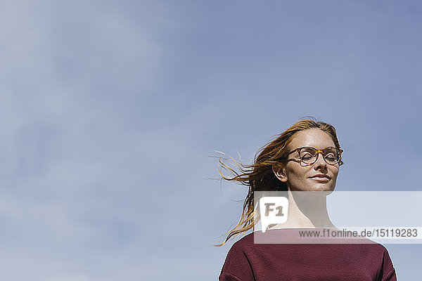 Porträt einer jungen Frau mit Brille und geschlossenen Augen unter blauem Himmel