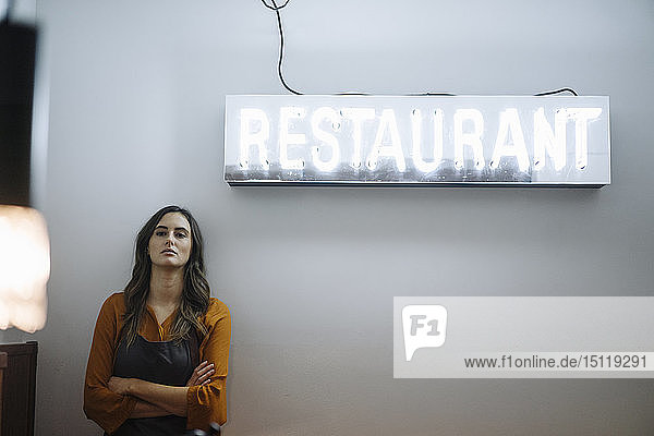 Serious young woman leaning against a wall under restaurant neon light