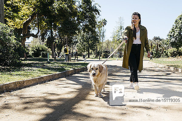 Glückliche Frau geht mit ihrem Labrador Retriever im Stadtpark spazieren