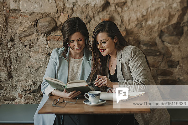 Zwei junge Frauen mit Notizbuch und Buch in einem Cafe