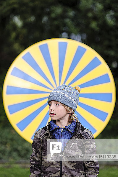 Porträt eines warm gekleideten Jungen  der vor einem gelb-blauen Kreis steht