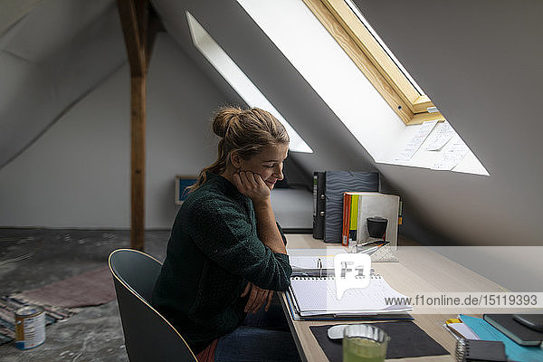 Junge Frau sitzt am Schreibtisch auf dem Dachboden und studiert Ordner