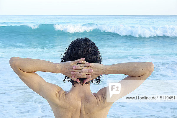 Seychellen  Rückenansicht eines Mannes mit Händen hinter dem Kopf vor dem Meer