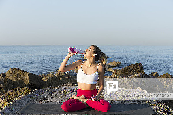 Junge Frau  die am Strand Yoga praktiziert  Trinkwasser