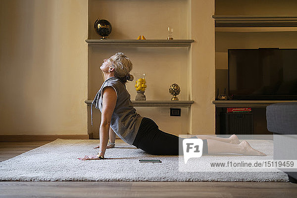 Reife Frau macht Yoga-Übung im Wohnzimmer