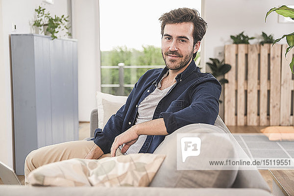 Young man sitting on couch at home  smiling