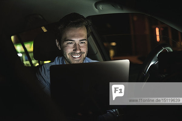 Smiling young man using laptop in car at night