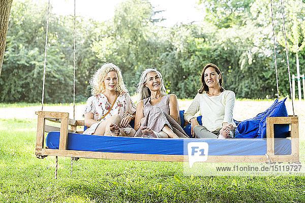 Frauen einer Familie  die sich im Garten entspannen und auf einem Schaukelbett sitzen