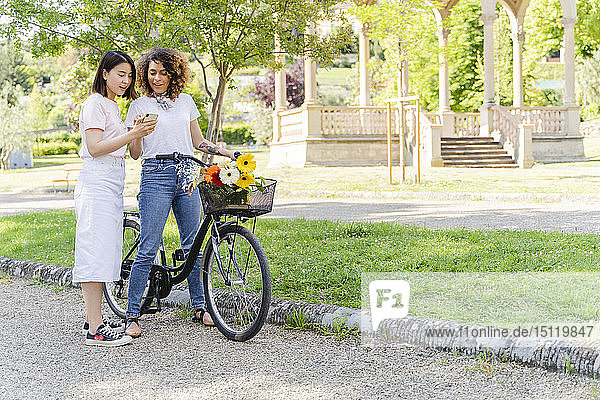 Two women with bicycle and cell phone in park