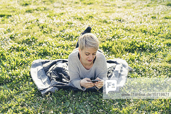 Junge Frau liegt auf einer Wiese und benutzt ein Smartphone