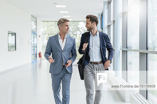 Two businessmen walking and talking in a passageway