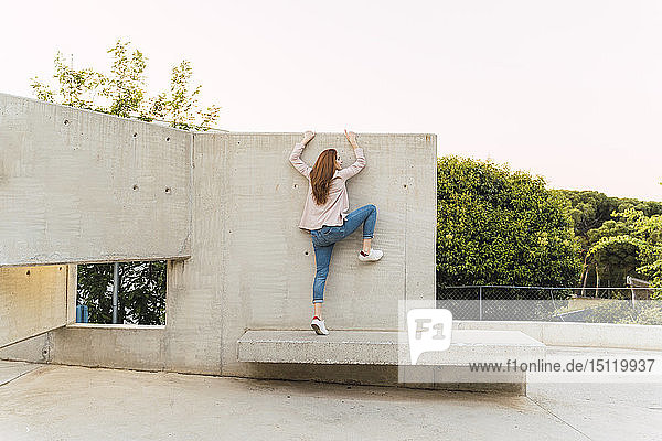 Young redheaded woman with raised arm on concrete bench