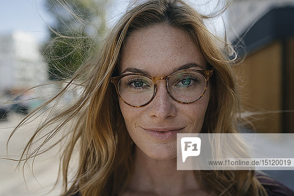 Porträt einer selbstbewussten jungen Frau mit Brille und windgepeitschtem Haar