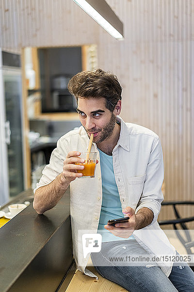 Mann mit Handy am Tresen einer Bar bei einem Drink