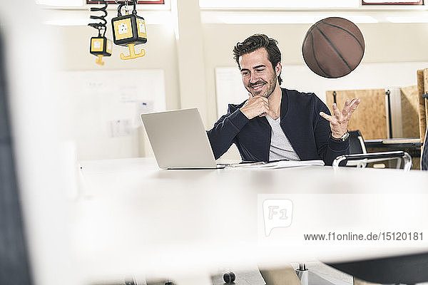 Young businessman using laptop  playing with a basketball