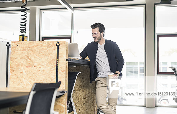 Young businessman in modern office using laptop on high desk