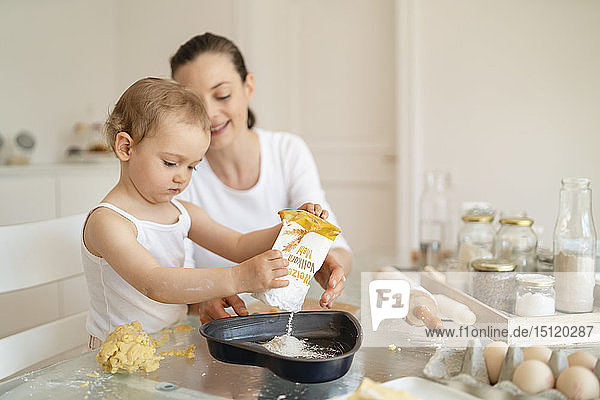 Mother and little daughter making a cake together in kitchen at home