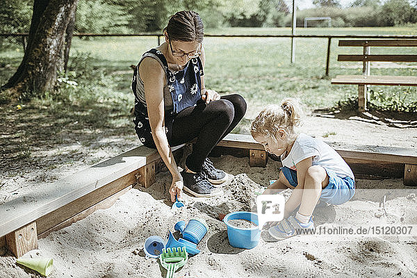 Mother playing with little daughter in sandbox on a playground