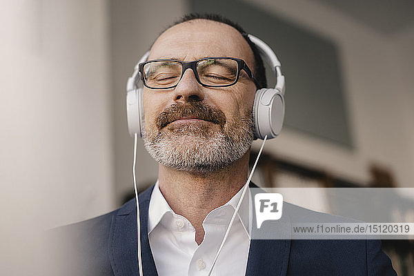 Mature businessman with closed eyes listening to music with headphones